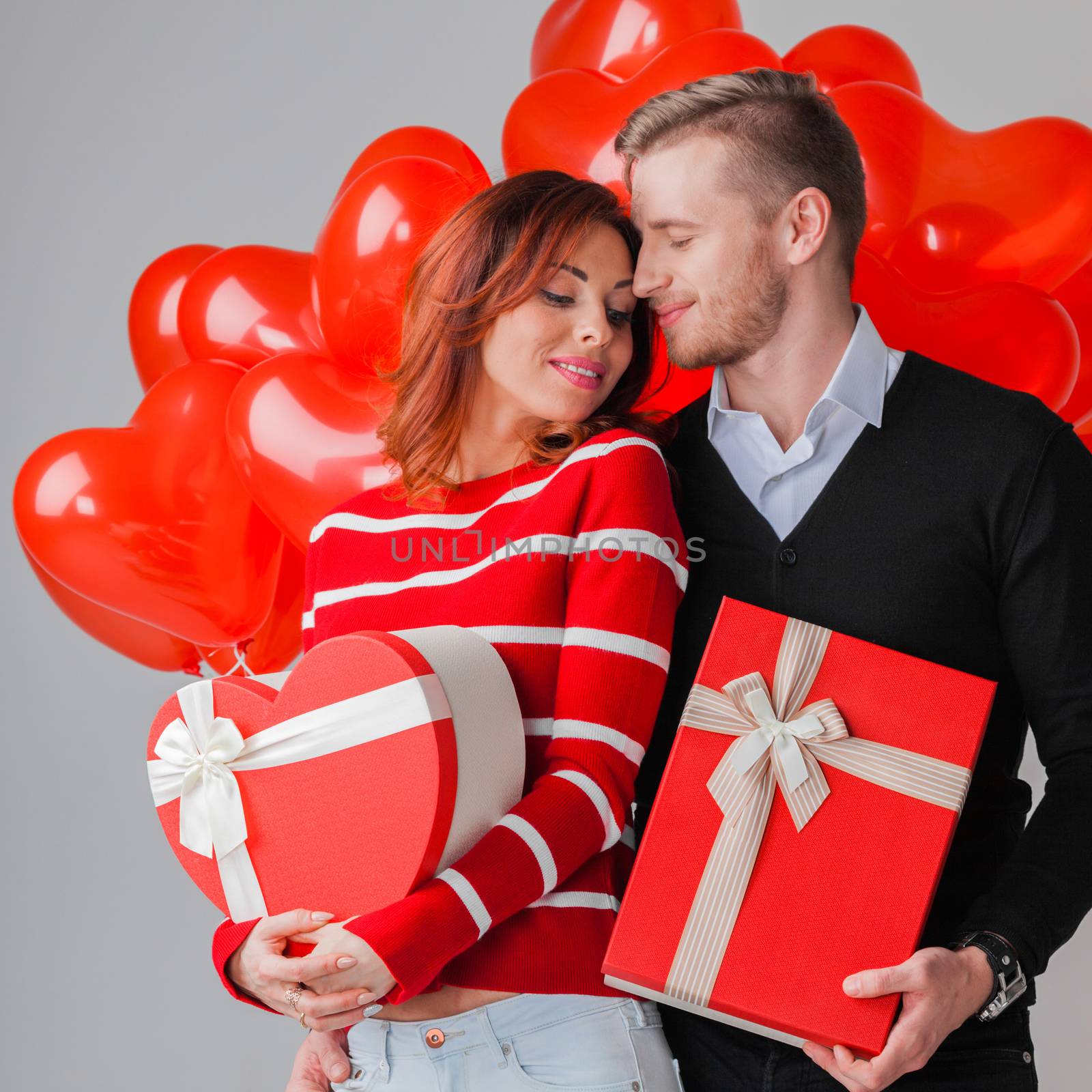 Happy embracing couple in love holding Valentines day gifts and bunch of heart shaped balloons
