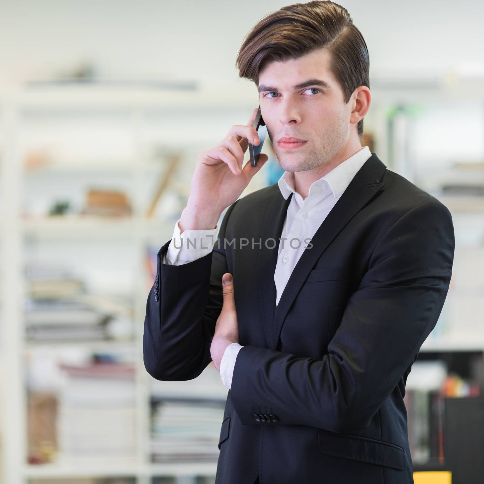 Portrait of hansome business man in office talking on mobile phone and looking at camera