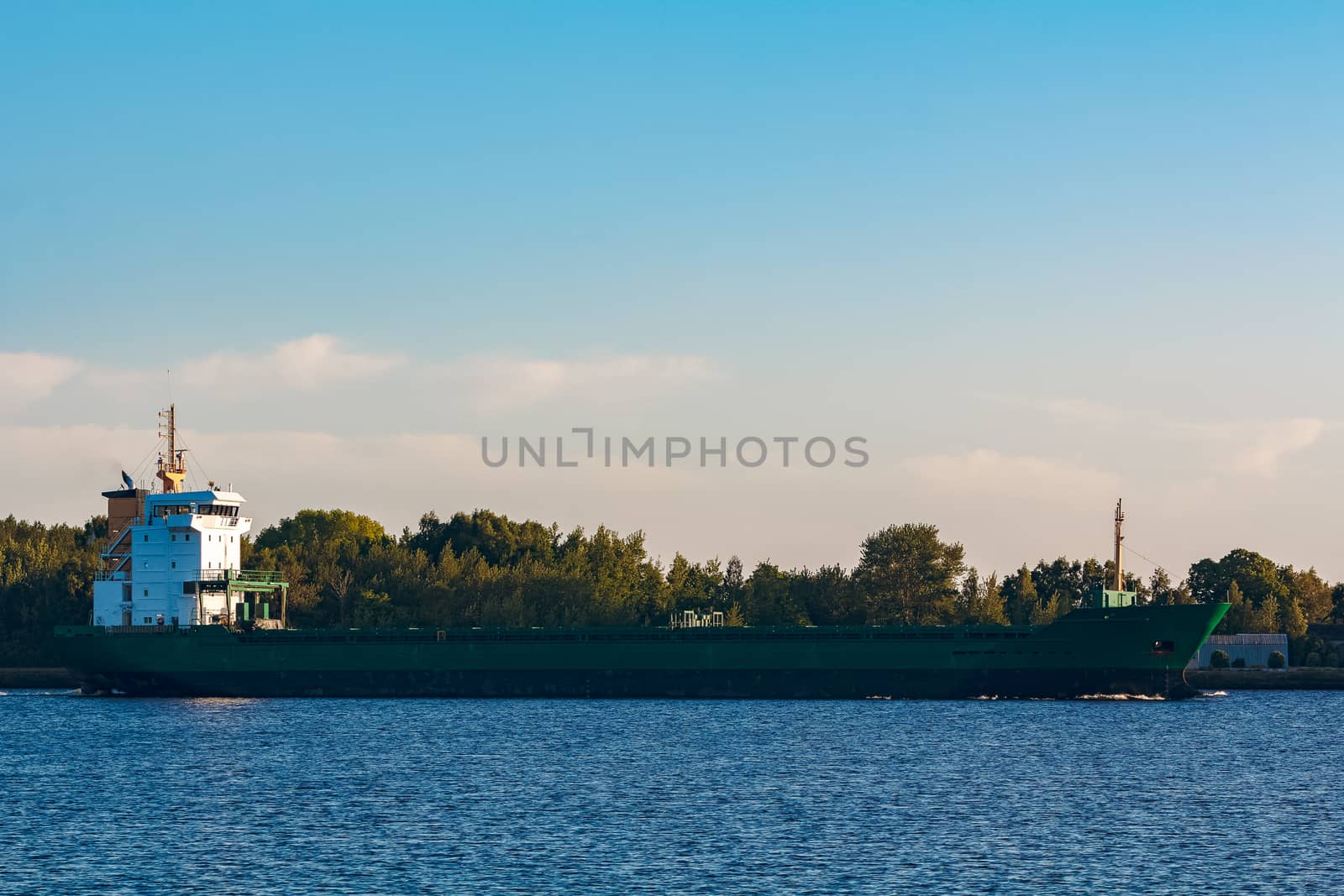 Green cargo ship leaves the port in a clear day