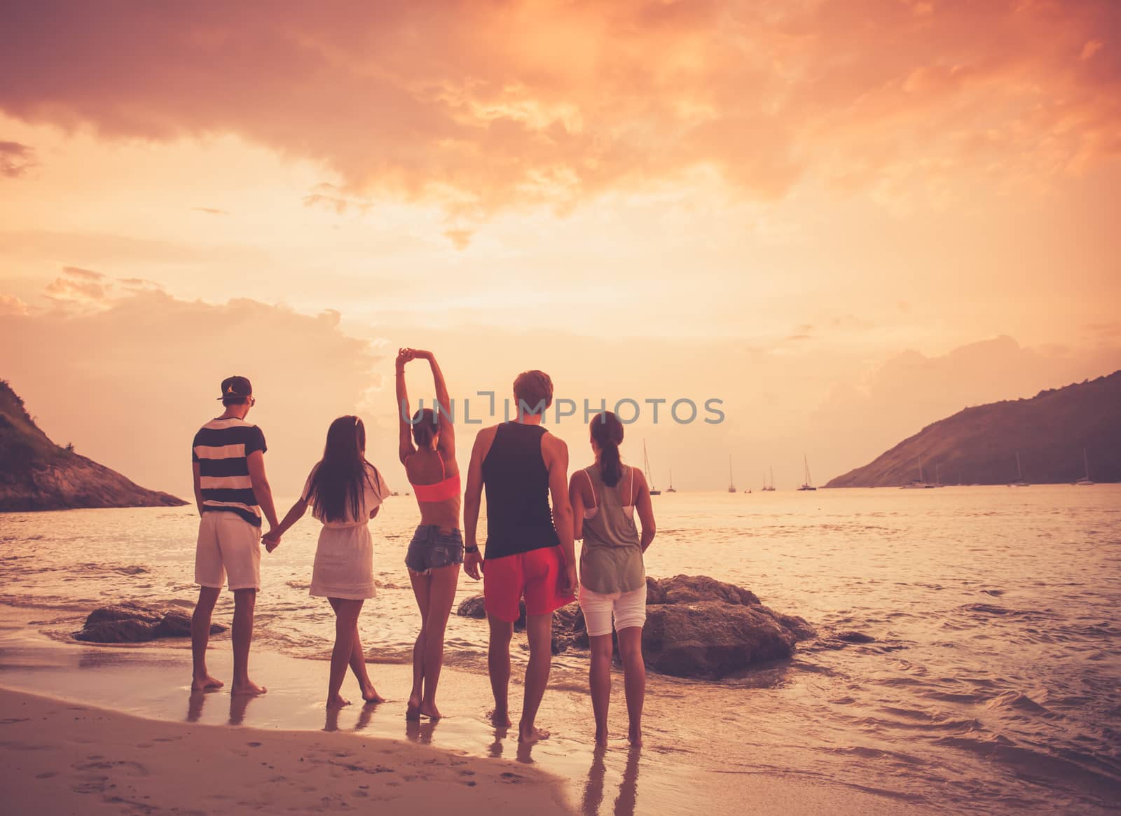 Group of happy people at sea beach at sunset