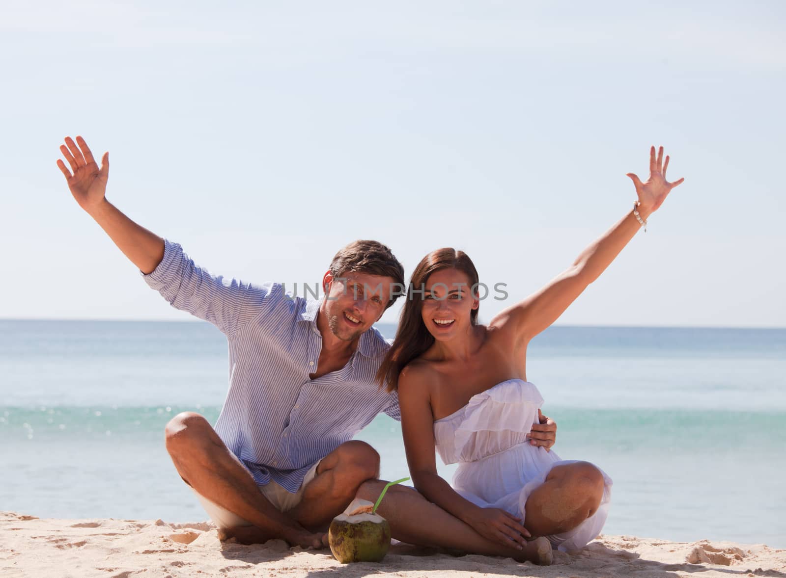 Cheerful couple sitting on beach and waving hands