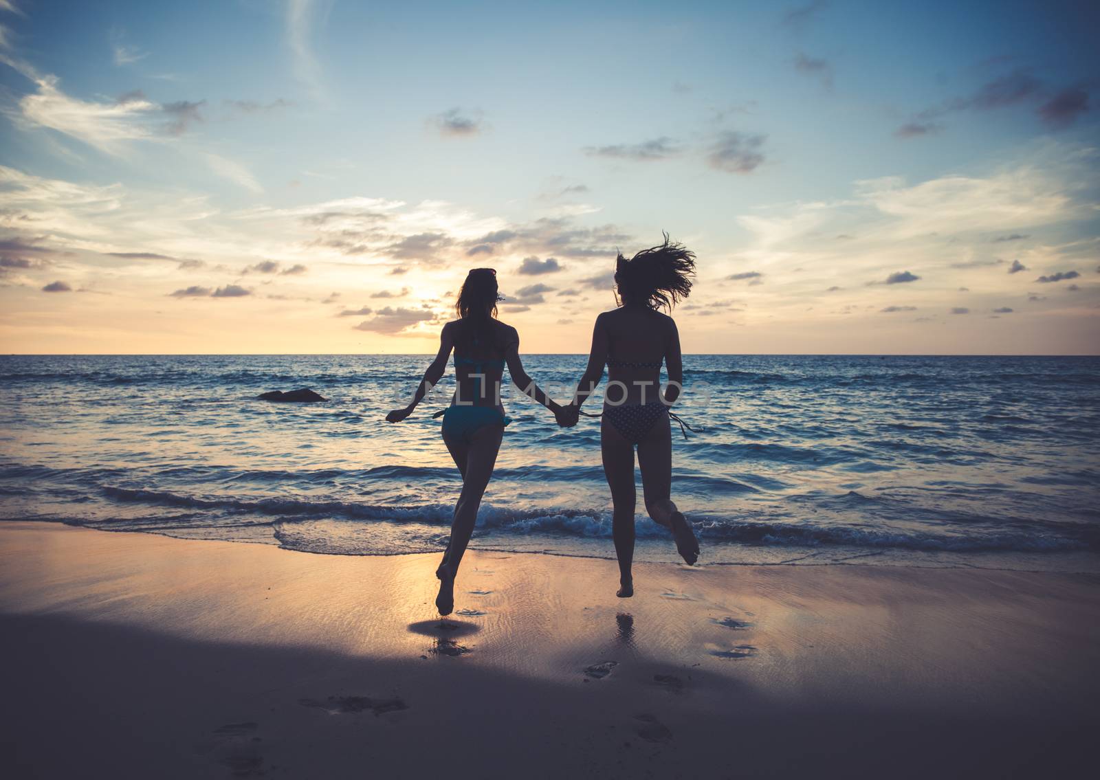 Happy female friends having fun on beach at sunset