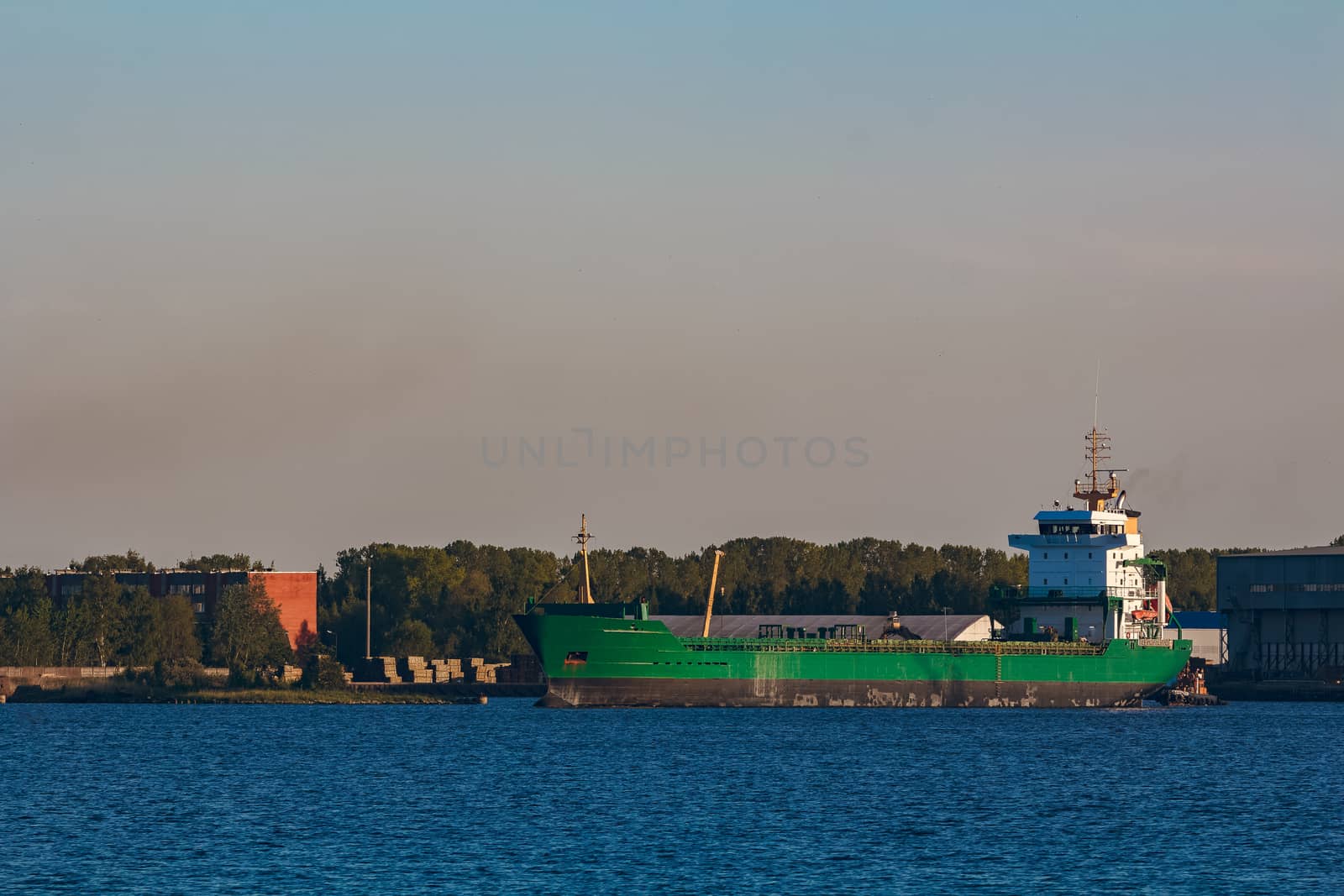 Green cargo ship leaves the port in a clear day