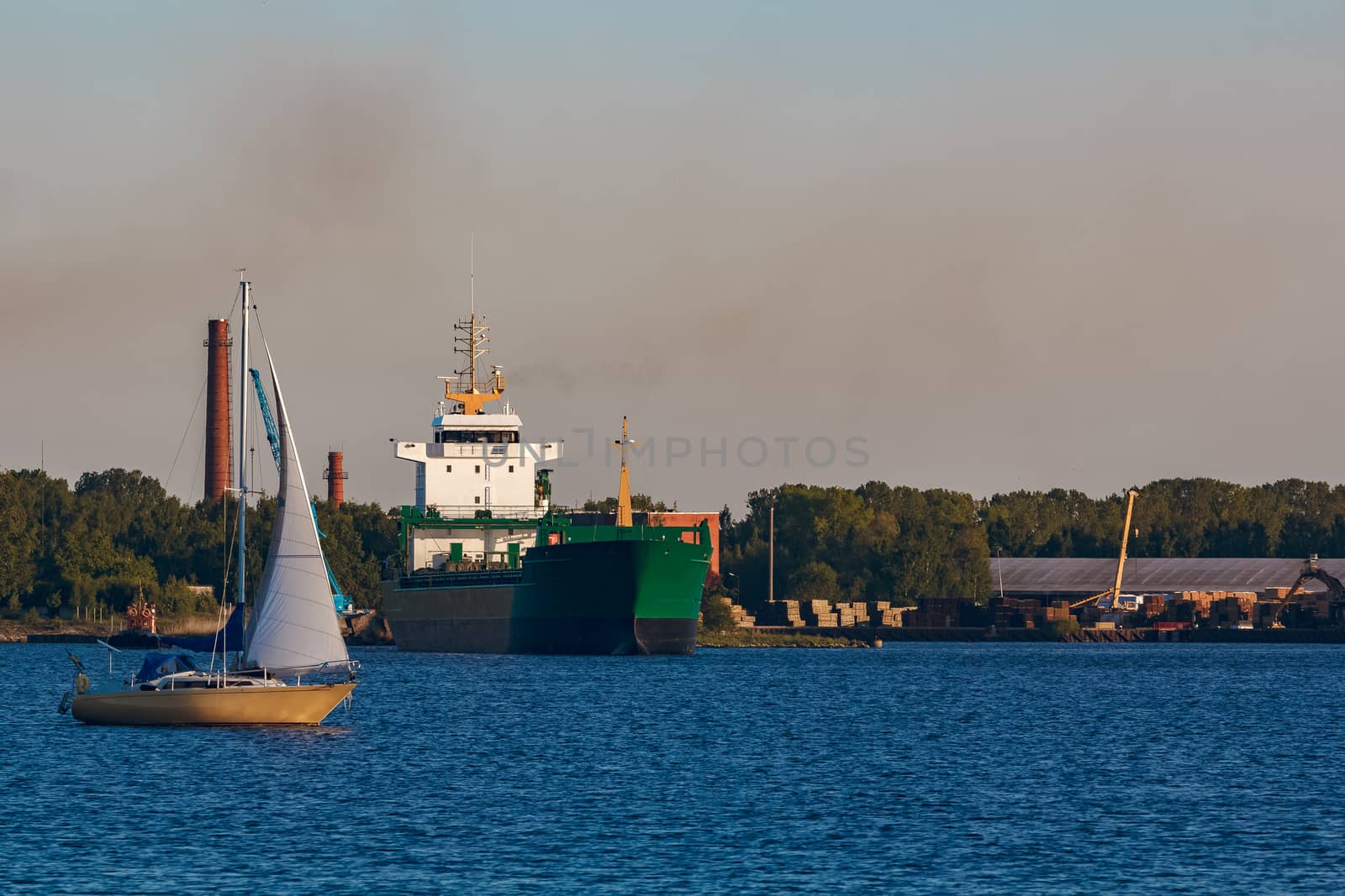 Green cargo ship leaves the port in a clear day