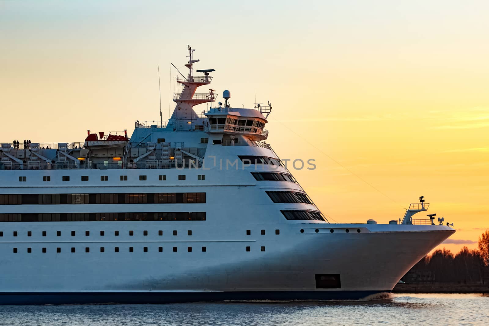 White passenger ship moving against the orange sunset sky