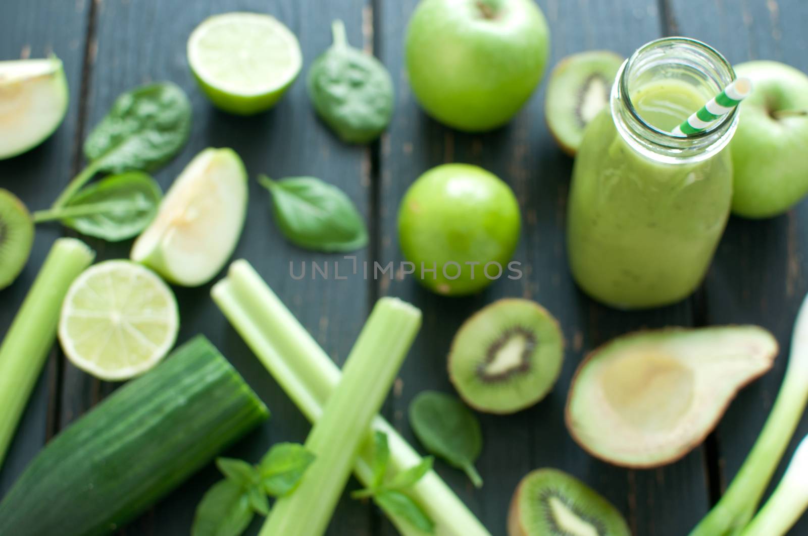 Fresh ingredients around a green smoothie bottle with straw
