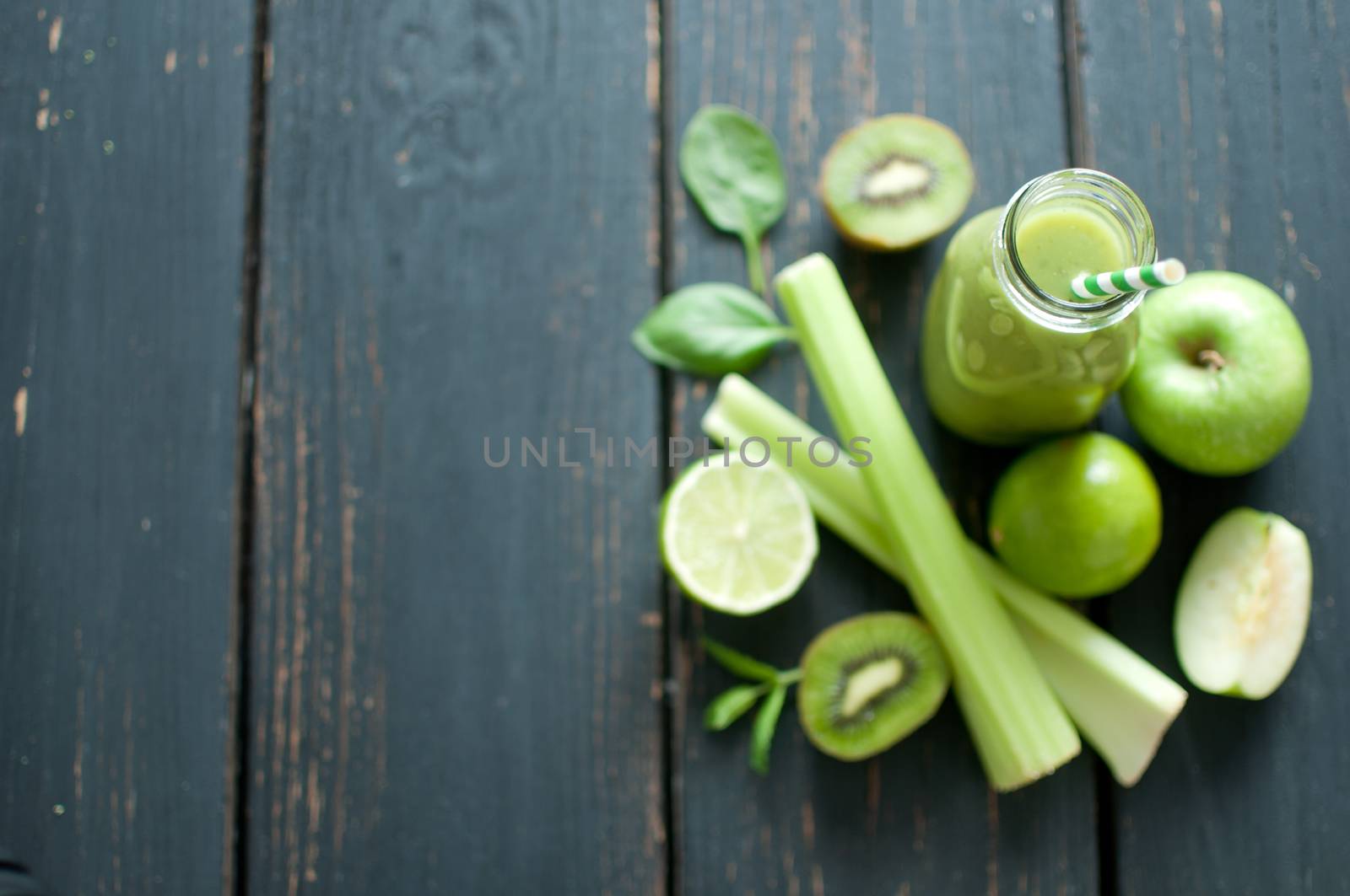 Green smoothie bottle with ingredients on wooden table 
