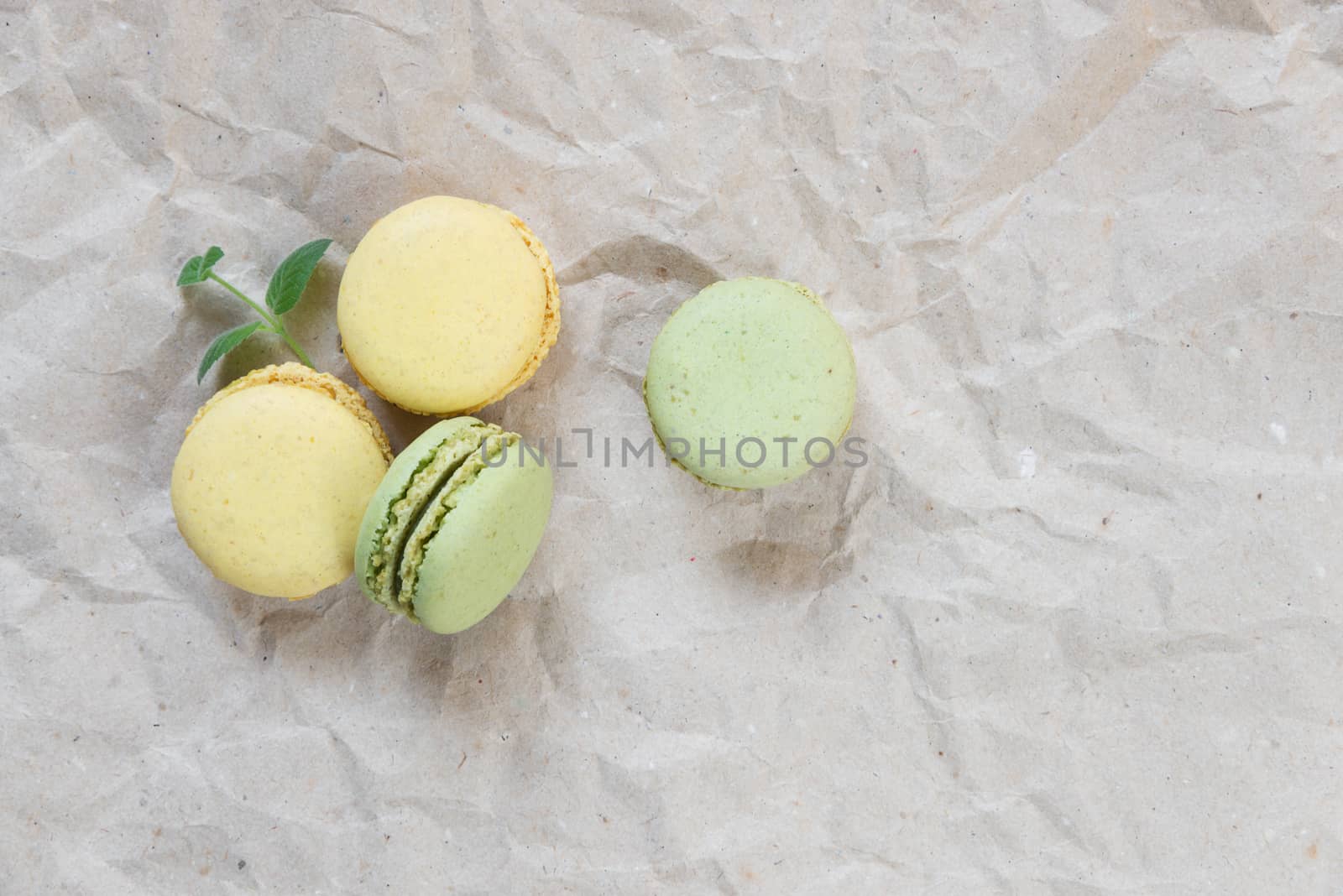 Green and yellow almond cookies (macaroons) and green mint leaves on the background of crumpled craft paper; top view, flat lay composition