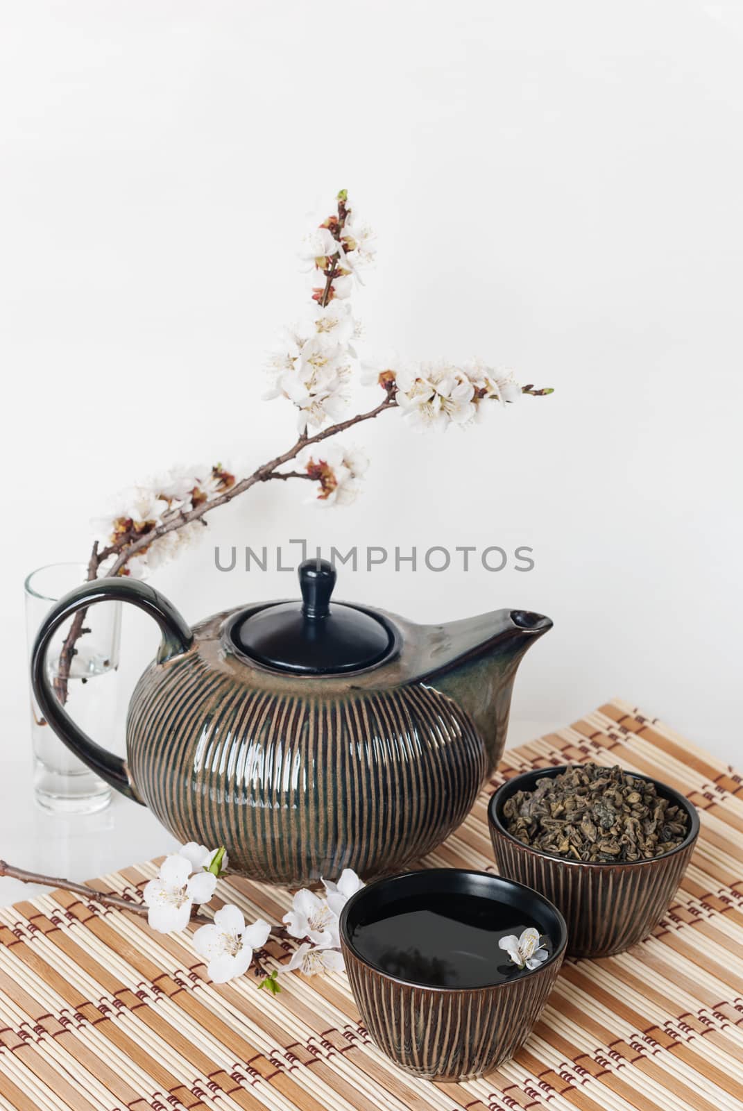 Still life in Japanese style: teapot, cups with green tea and blooming cherry twig