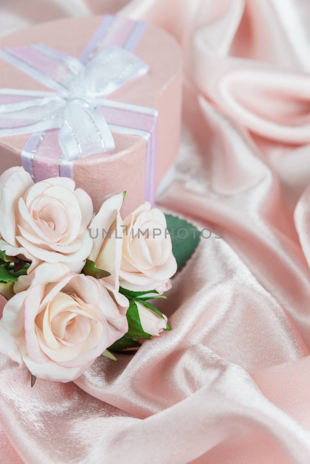 Pink roses and gift box with bow on a background of the silk fabric, vertical image