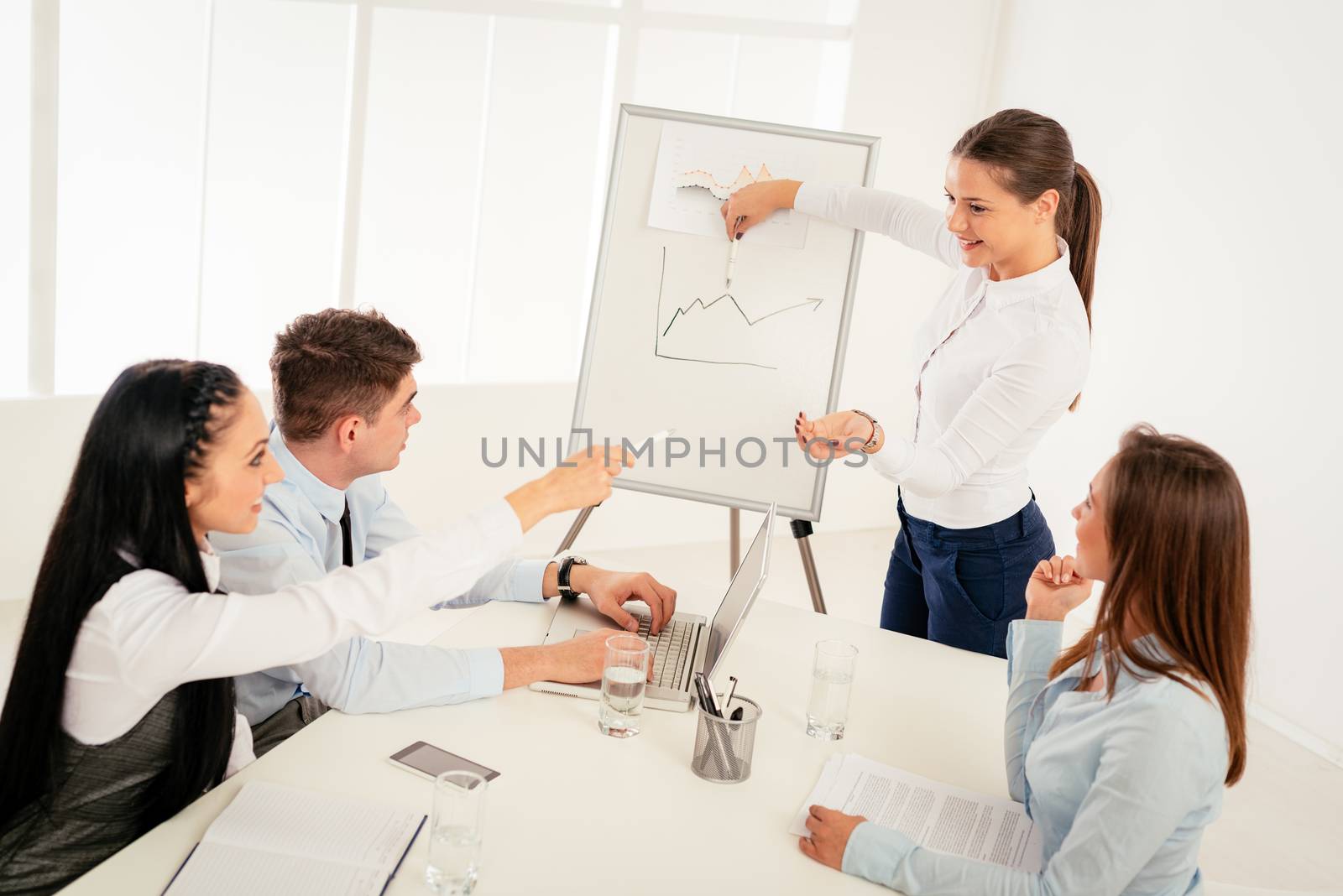 Businesspeople having meeting in a office. Young businesswoman standing  in front of flip chart and having presentation.