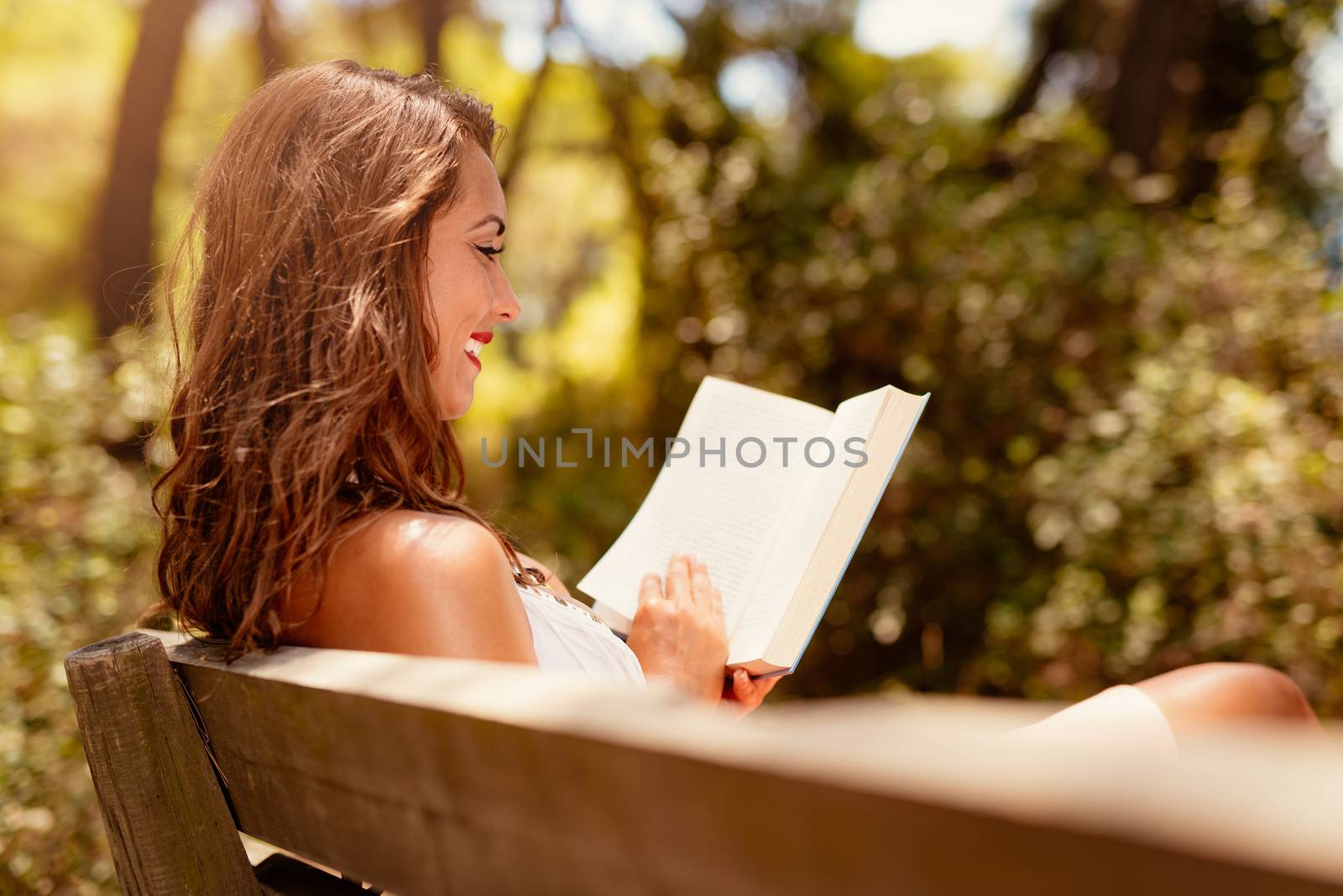 Young woman reading a book while relaxing in the sunny forest.