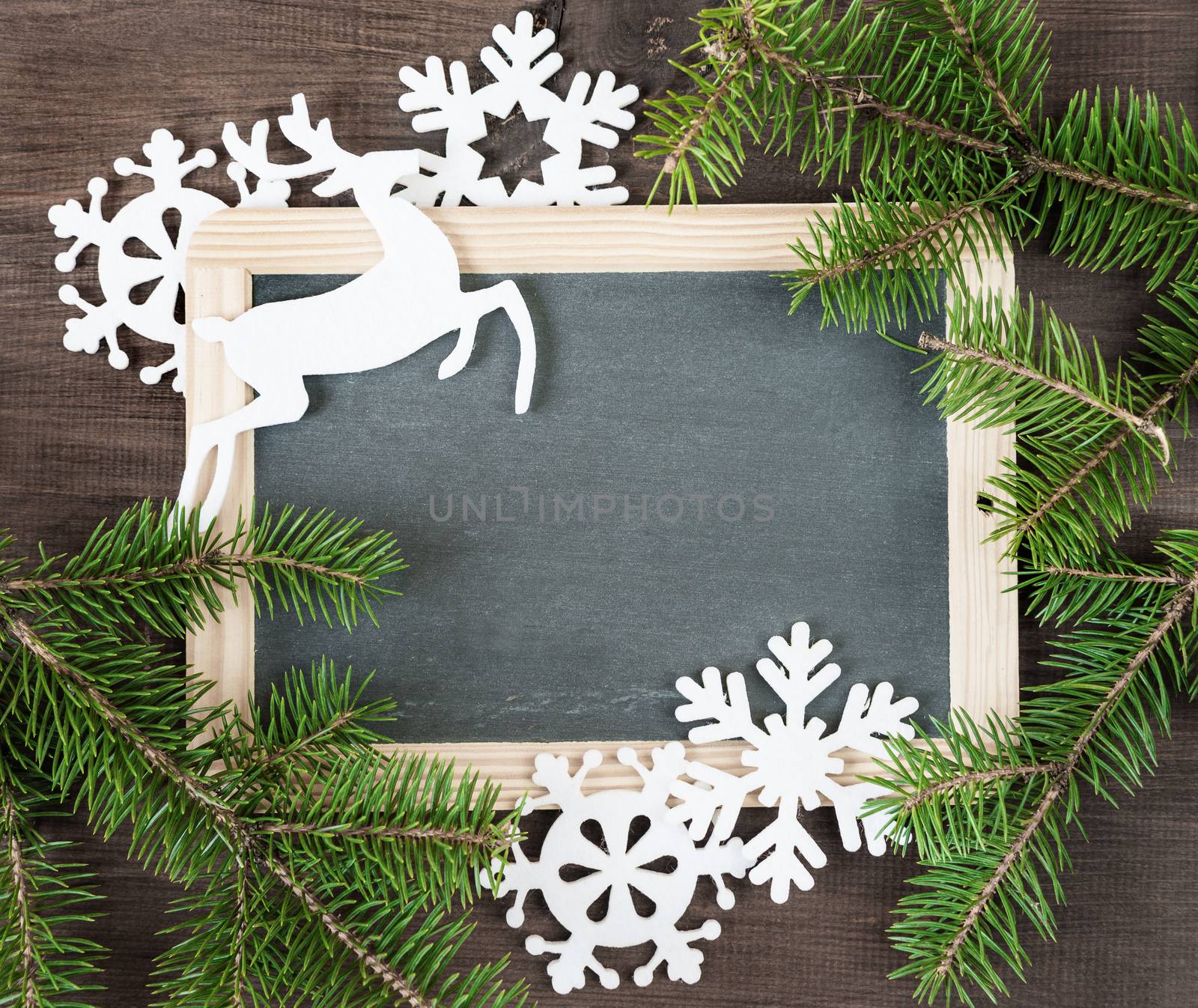 Christmas background: blank chalkboard surrounded by green fir branches and white felts snowflakes and deer