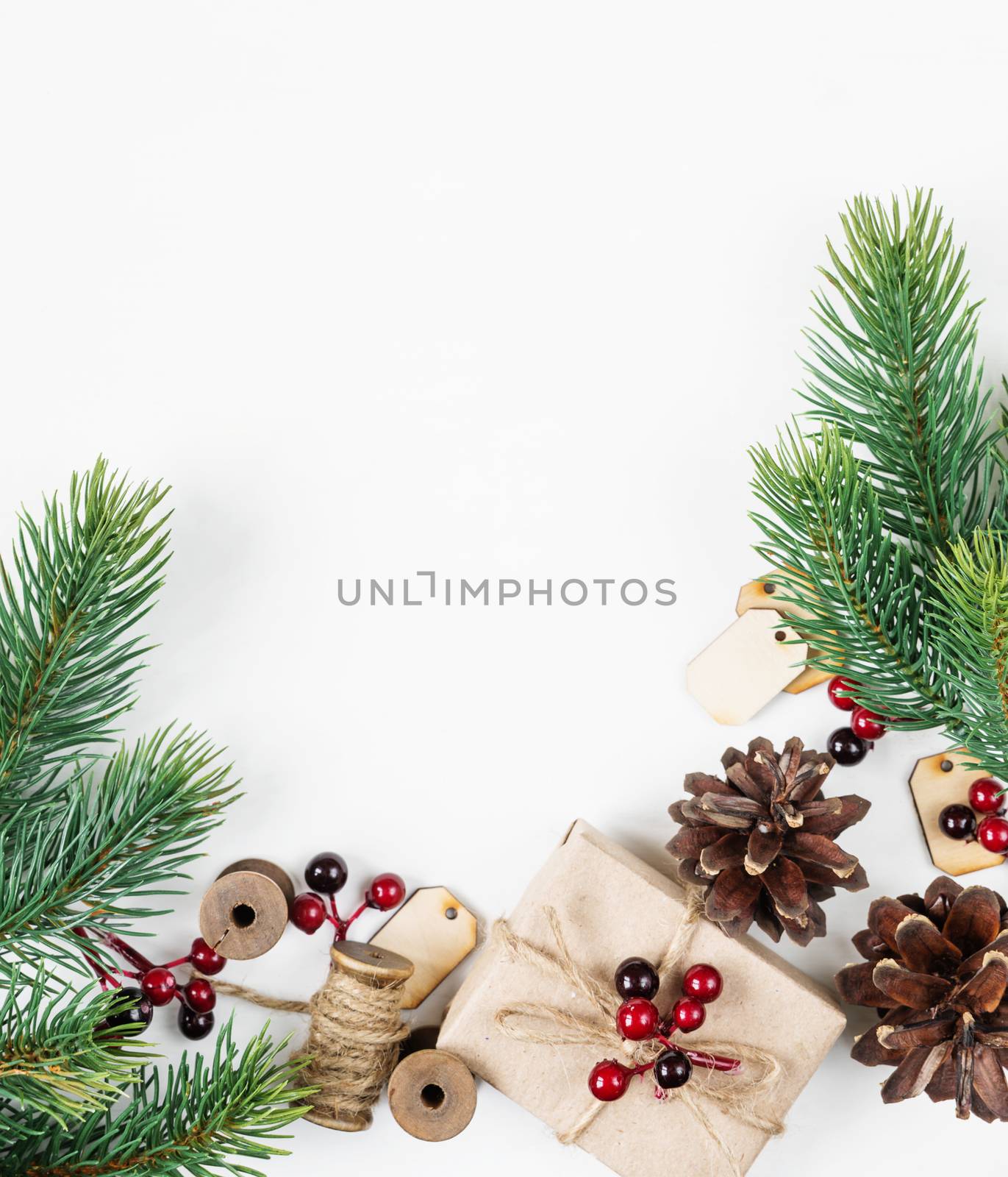 Christmas frame, consisting of fir branches, cones, red holly berries and gift boxe tied with hemp twine on a white background with space for text. Flat lay composition for greeting cards, websites, social media, magazines, bloggers, artists etc. Christmas wallpaper