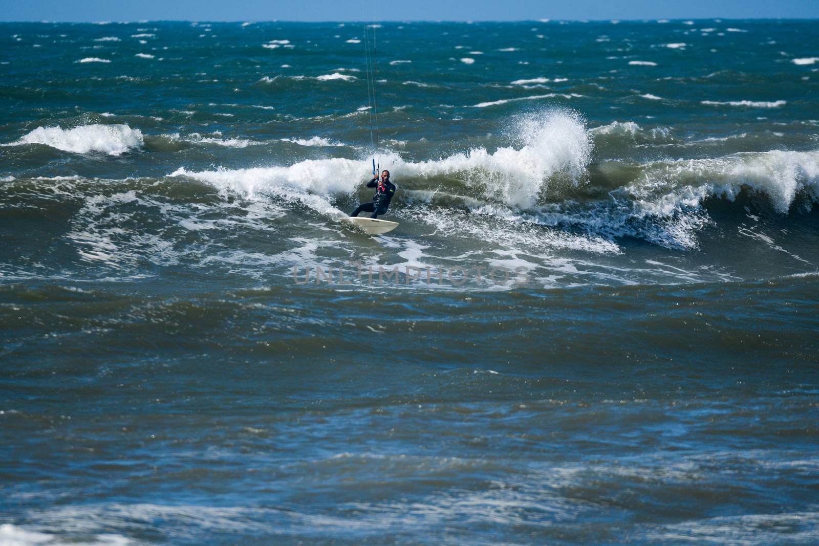 Kitesurfer riding ocean waves on a bright sunny day.