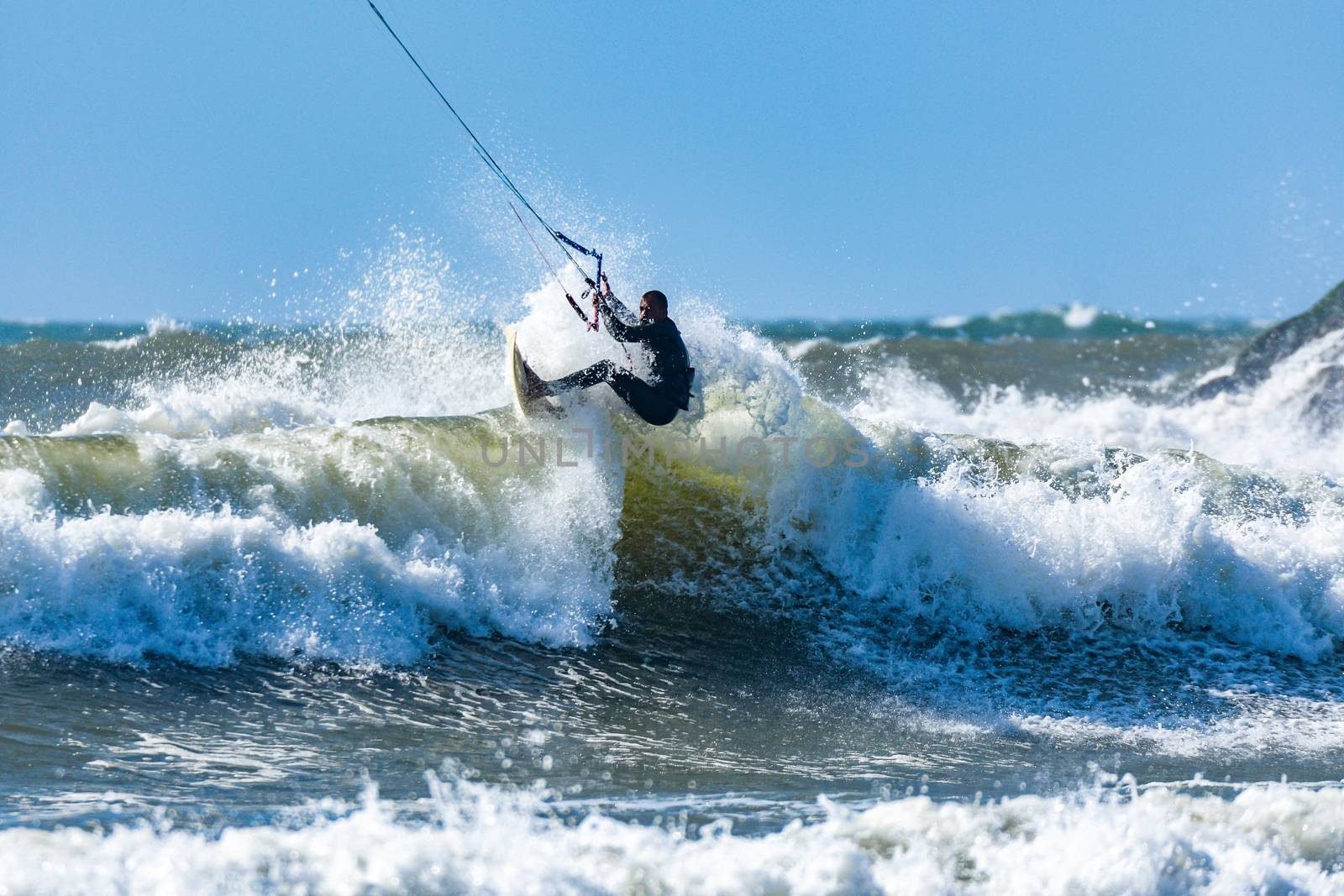 Kitesurfer riding ocean waves on a bright sunny day.