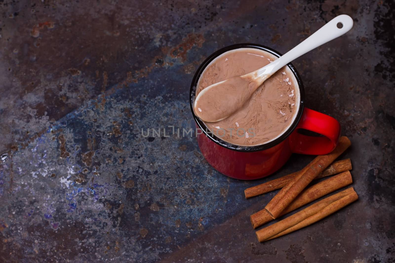 Vintage mug of hot chocolate with cinnamon sticks over dark background.