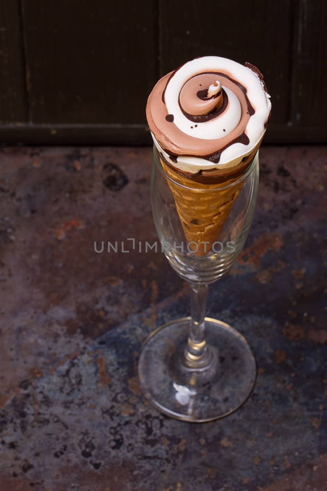 Ice cream in waffle cone with chocolate syrup toppingn in glass on dark black background