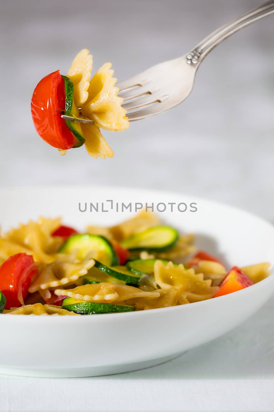 Whole farfalle pasta with zucchini, cherry tomatoes and red onion suspended on the fork