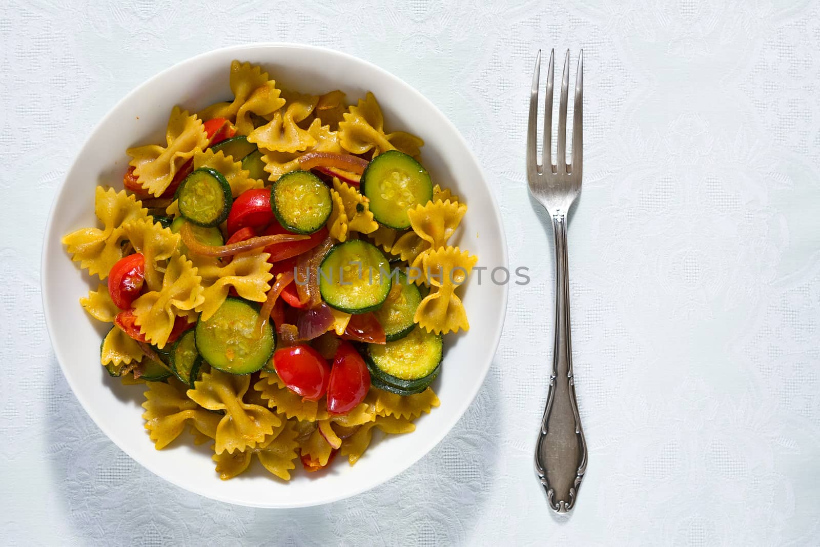 Whole farfalle pasta with zucchini, cherry tomatoes and red onion seen from above