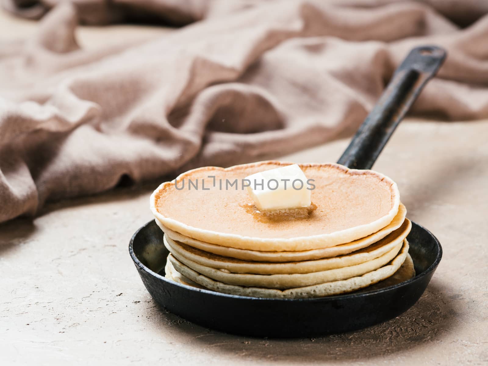 homemade pancakes with butter in iron cast. Stack of pancakes on brown concrete background. Close up.