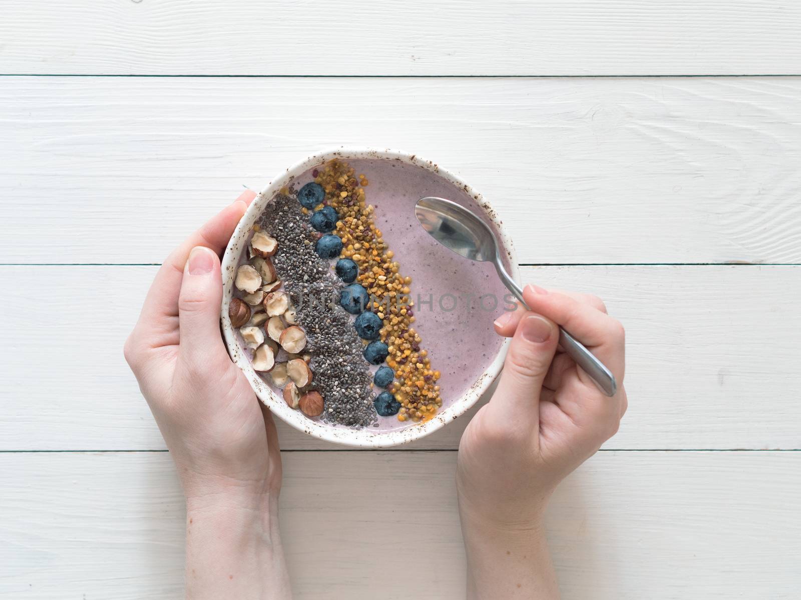 Eating healthy breakfast bowl. Buckwheat smoothie porrige, fresh berries, seeds and nuts, bee pollen in white ceramic bowl in woman hands on table. Clean eating, dieting,detox, vegetarian food concept