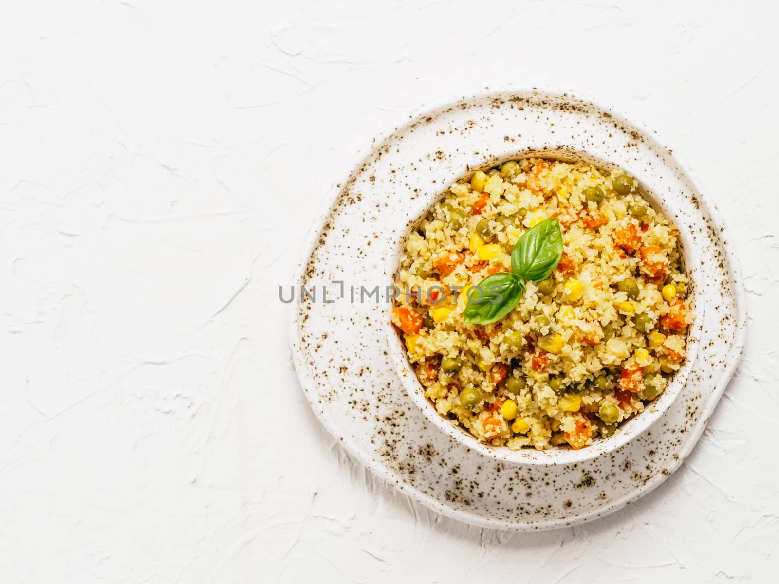 Top view of cauliflower rice with vegetables. Organic paleo Cauliflower Rice with corn, green peas and carrots on white concrete background. Copy space.