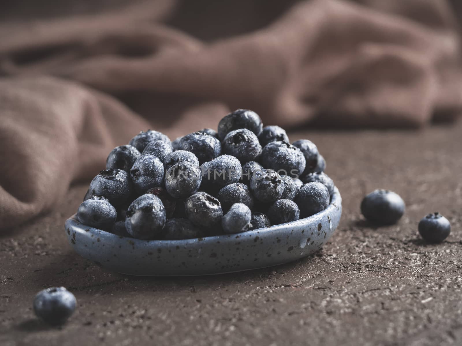 Blueberries in plate on brown concrete background. Fresh picked bilberries close up. Copyspace. Close up