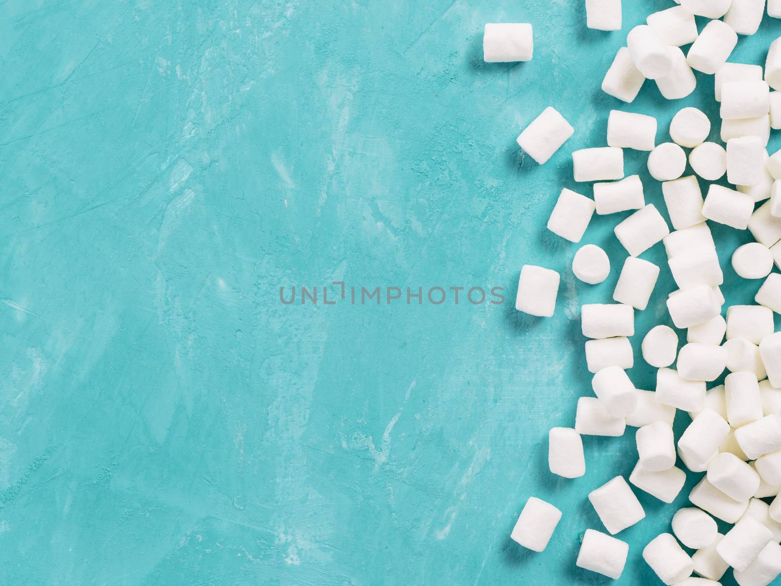 Marshmallows on blue background with copyspace. Flat lay or top view. Background or texture of colorful mini marshmallows. Winter food background concept.