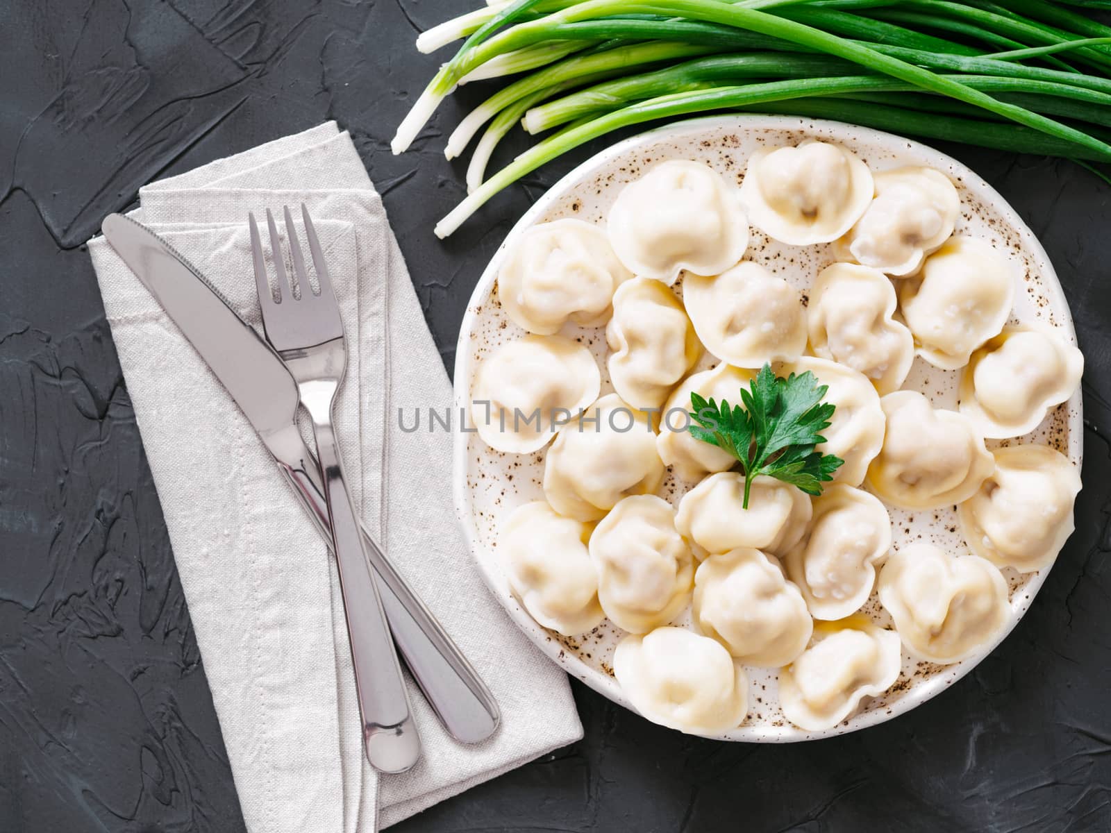 Traditional russian pelmeni, ravioli, dumplings with meat on black concrete background. Top view or flat lay. Russian food and russian kitchen concept.