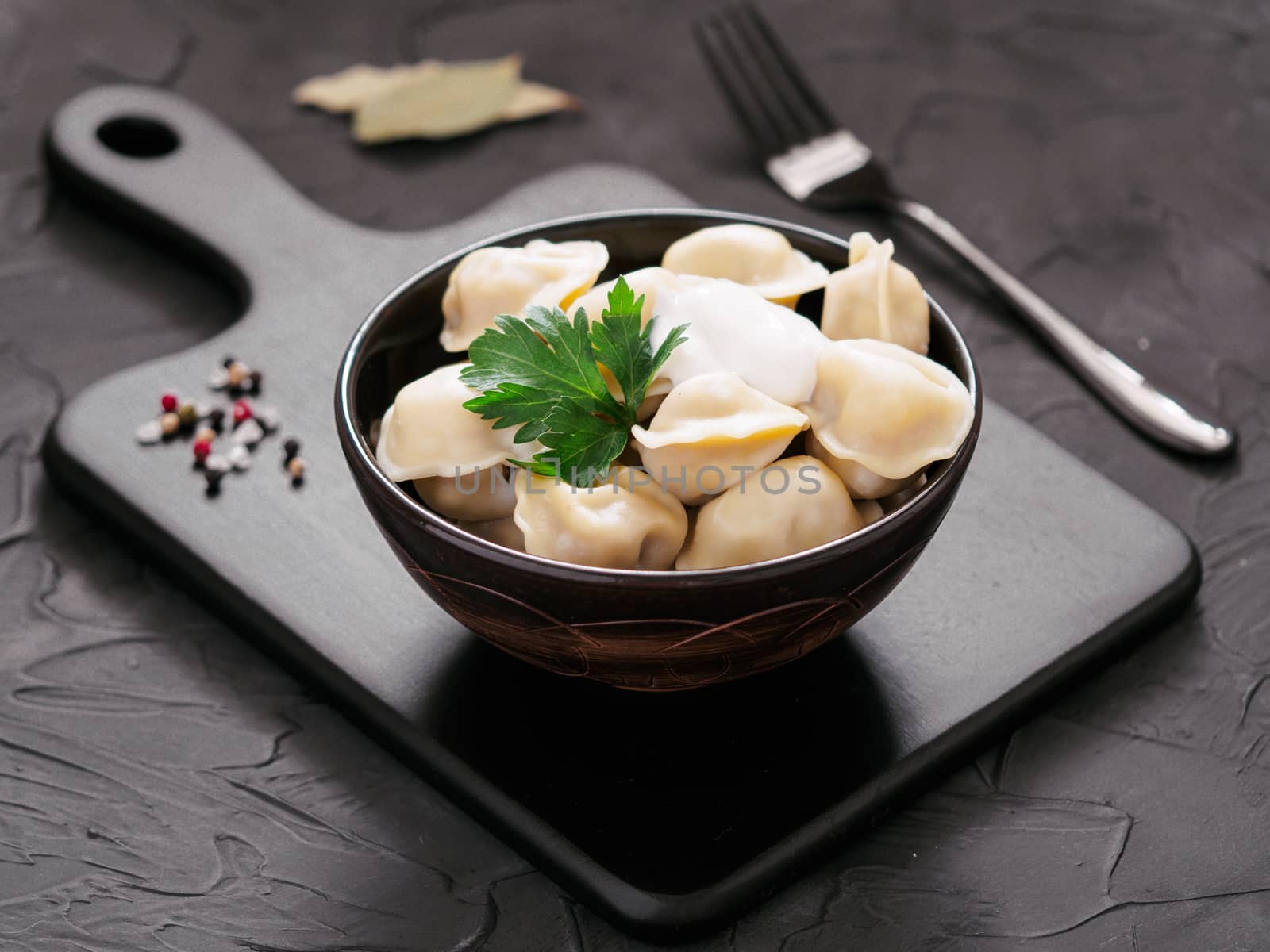 Traditional russian pelmeni, ravioli, dumplings with meat on black cutting board over black concrete background. Russian food and russian kitchen concept.