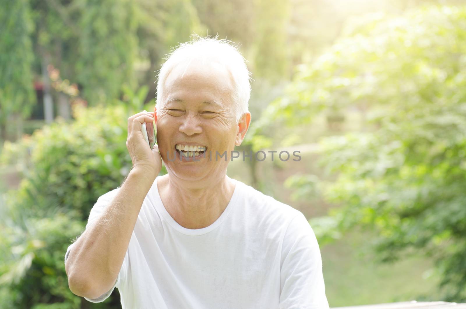 Portrait of happy gray hair Asian old man talking on smart phone, at outdoor park in morning. 
