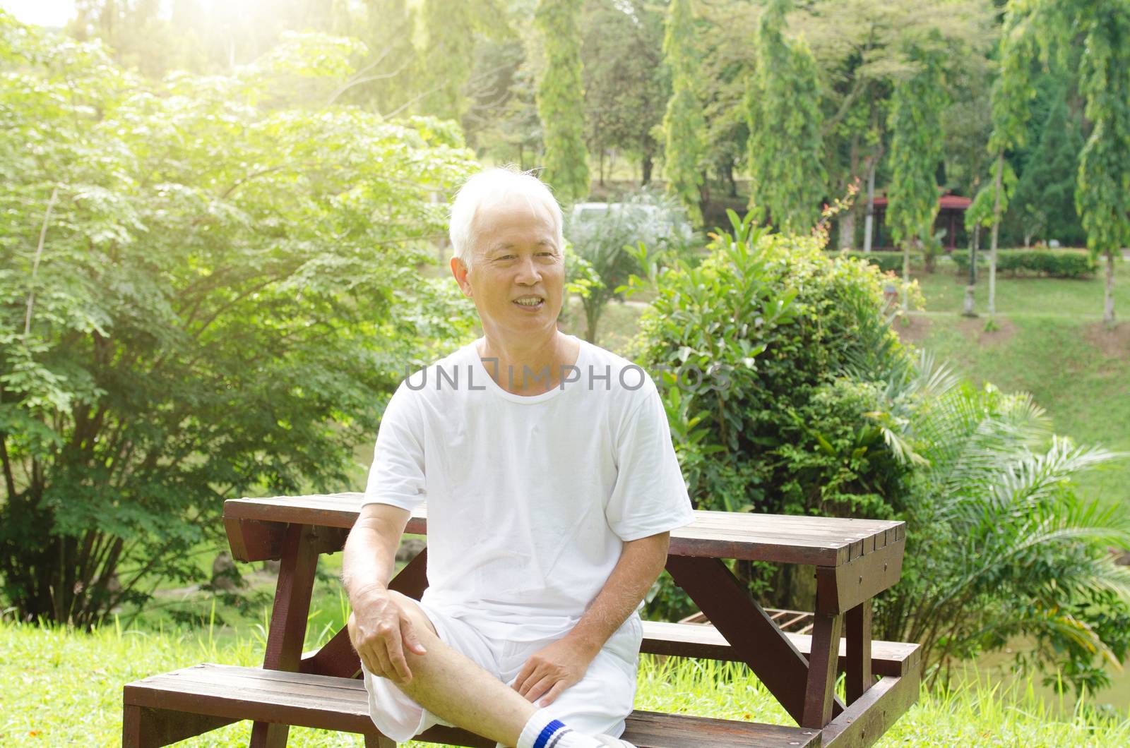 Portrait of white hair Asian old man smiling, sitting at outdoor park in morning. 