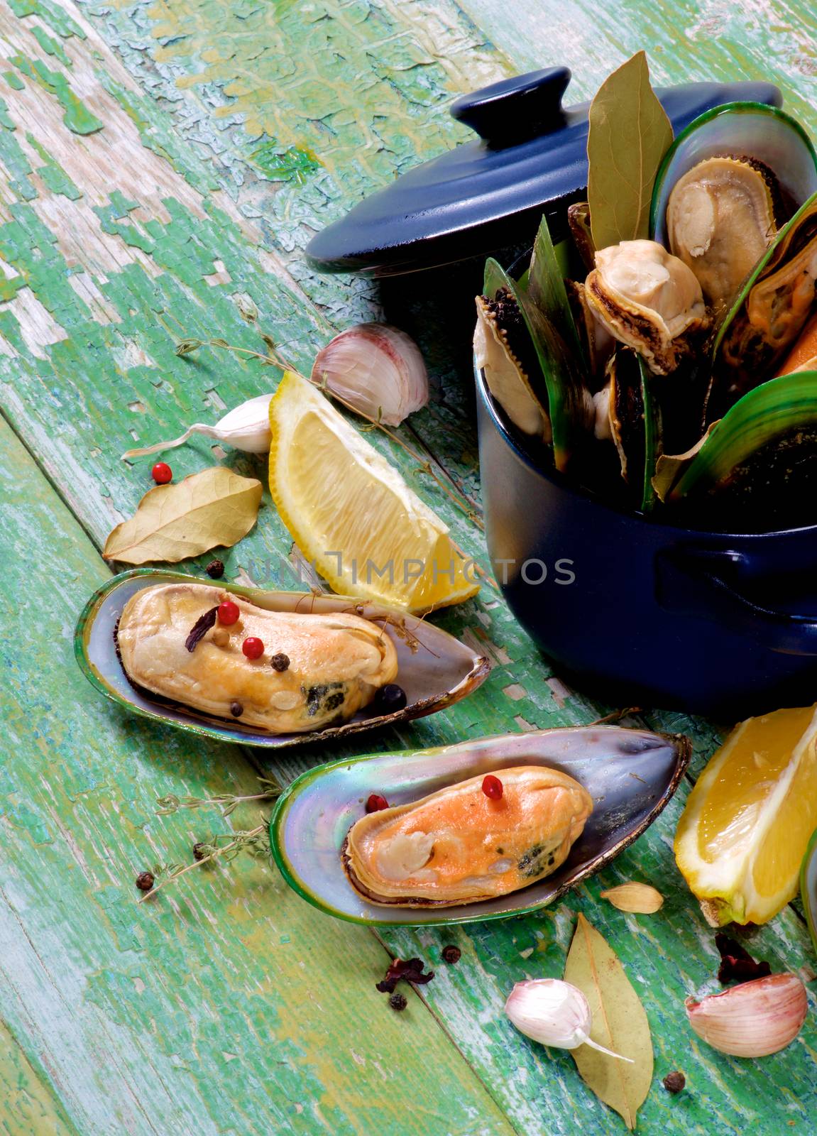 Arrangement of Fresh Boiled Green Mussels with Spices and Lemon in Dark Saucepan closeup on Green Wooden background