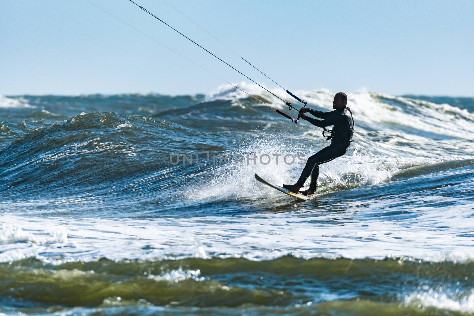 Kitesurfer riding ocean waves on a bright sunny day.