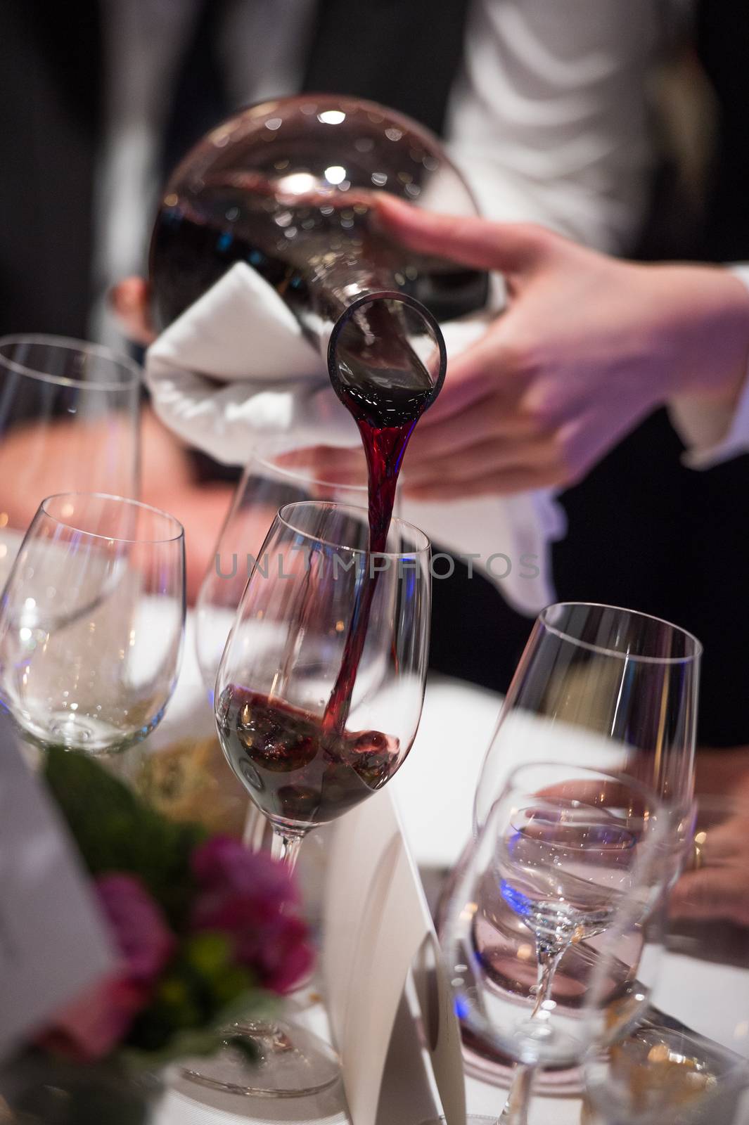 Sommelier pouring wine into glass from mixing bowl at luxury diner