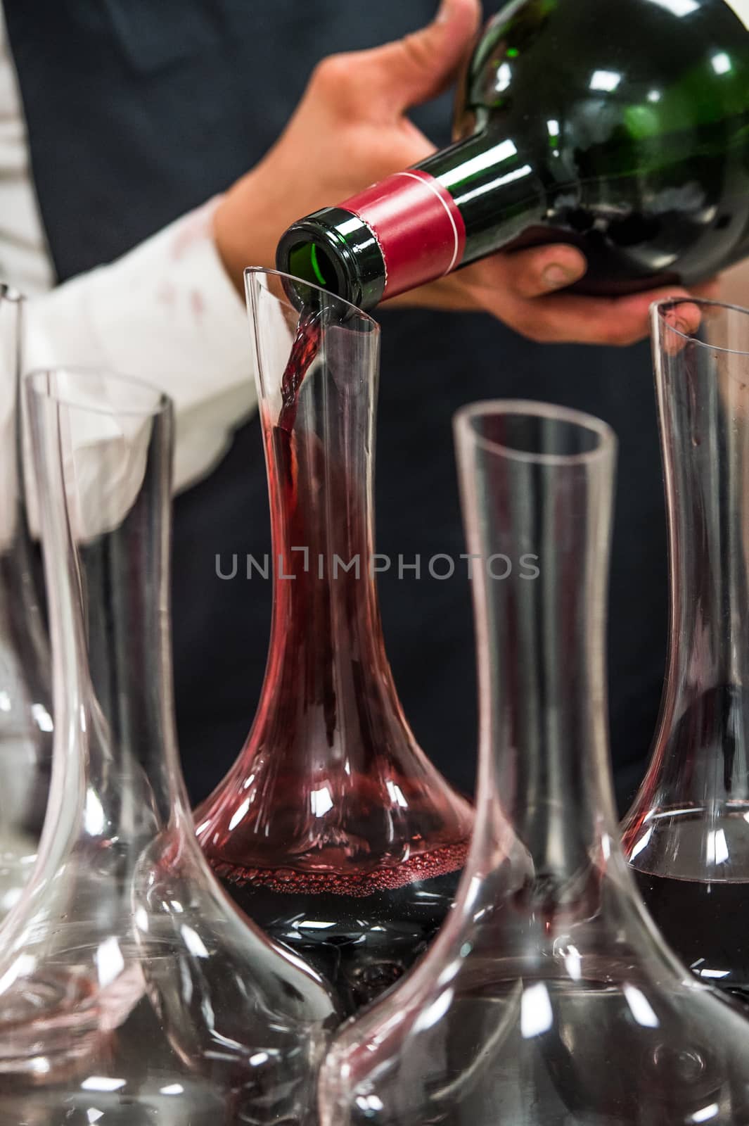 Sommelier at work, pouring wine to decanter while standing near the wine shelf, Luxury Diner