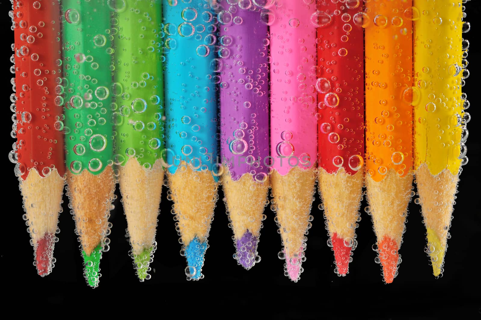 Color pencils isolated on black background into water with bubbles. Close up