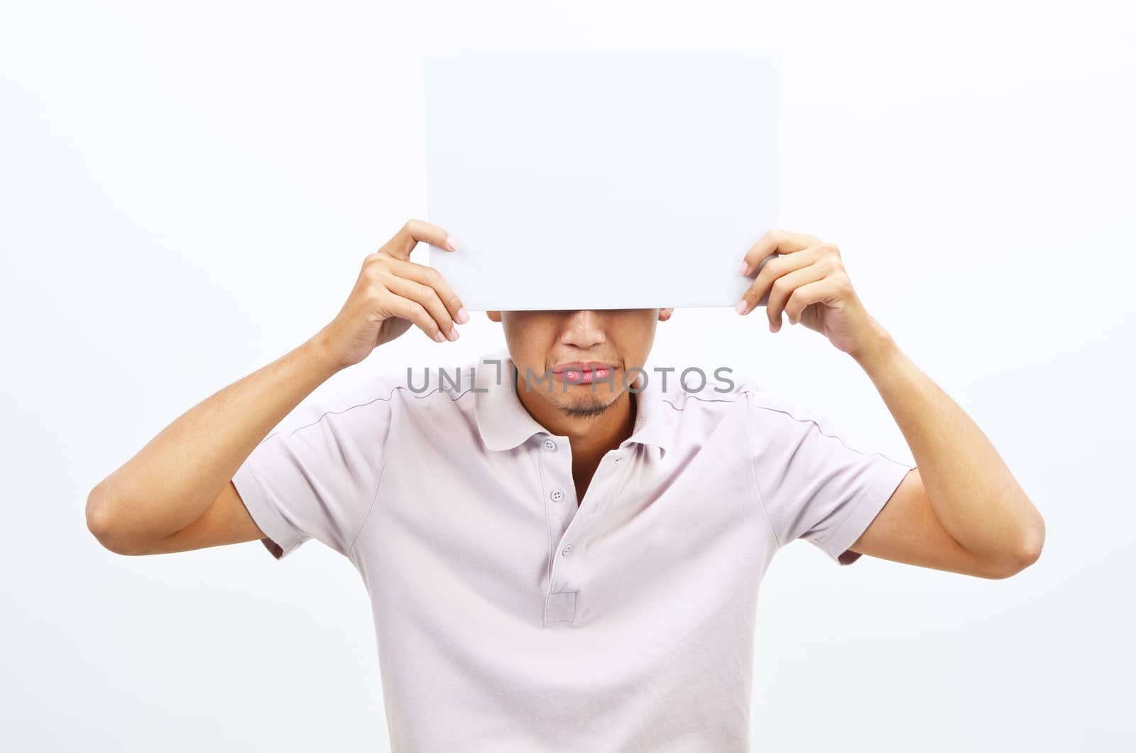 Portrait of sad Asian man hand holding white blank paper card covering his eyes, standing isolated on plain background.