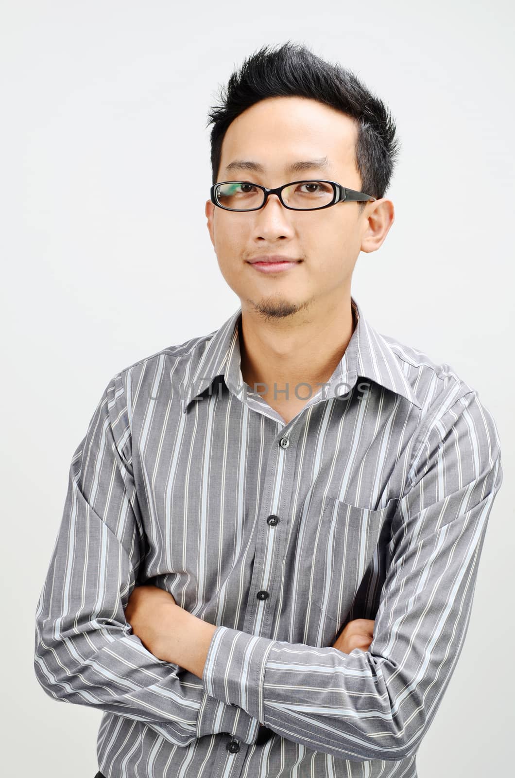 Portrait of Asian businessman arms crossed and smiling, standing isolated on plain background.