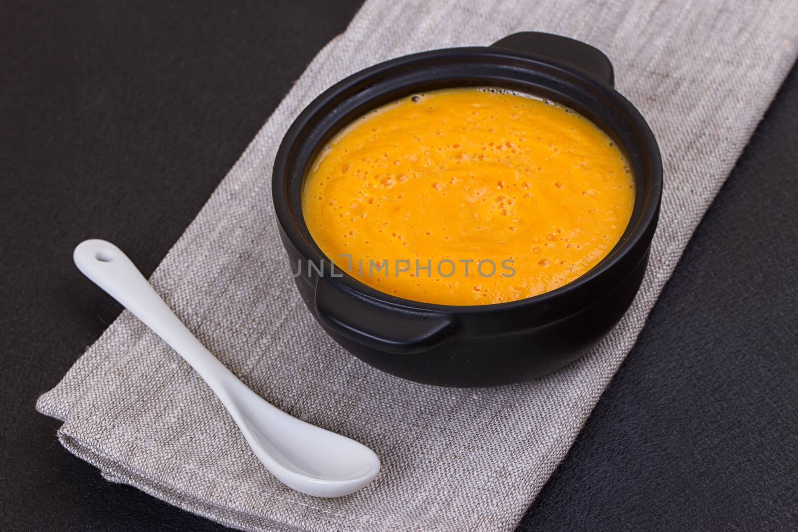 Pumpkin and carrot soup with cream and parsley on dark background