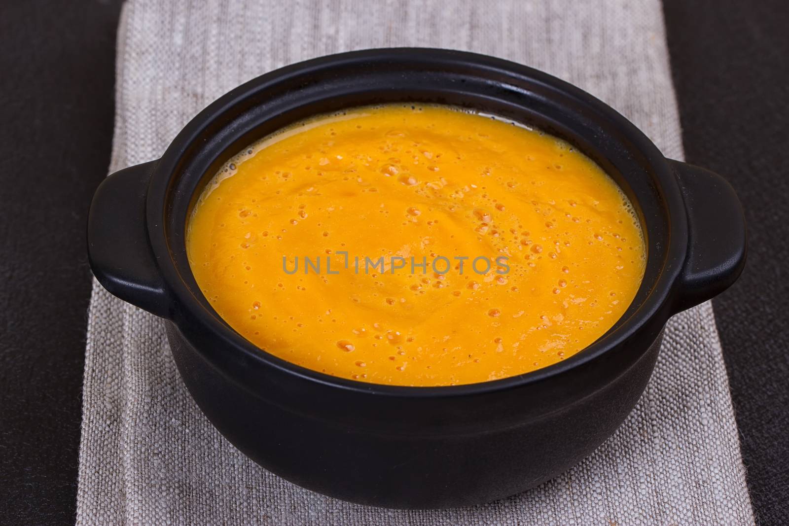 Pumpkin and carrot soup with cream and parsley on dark background