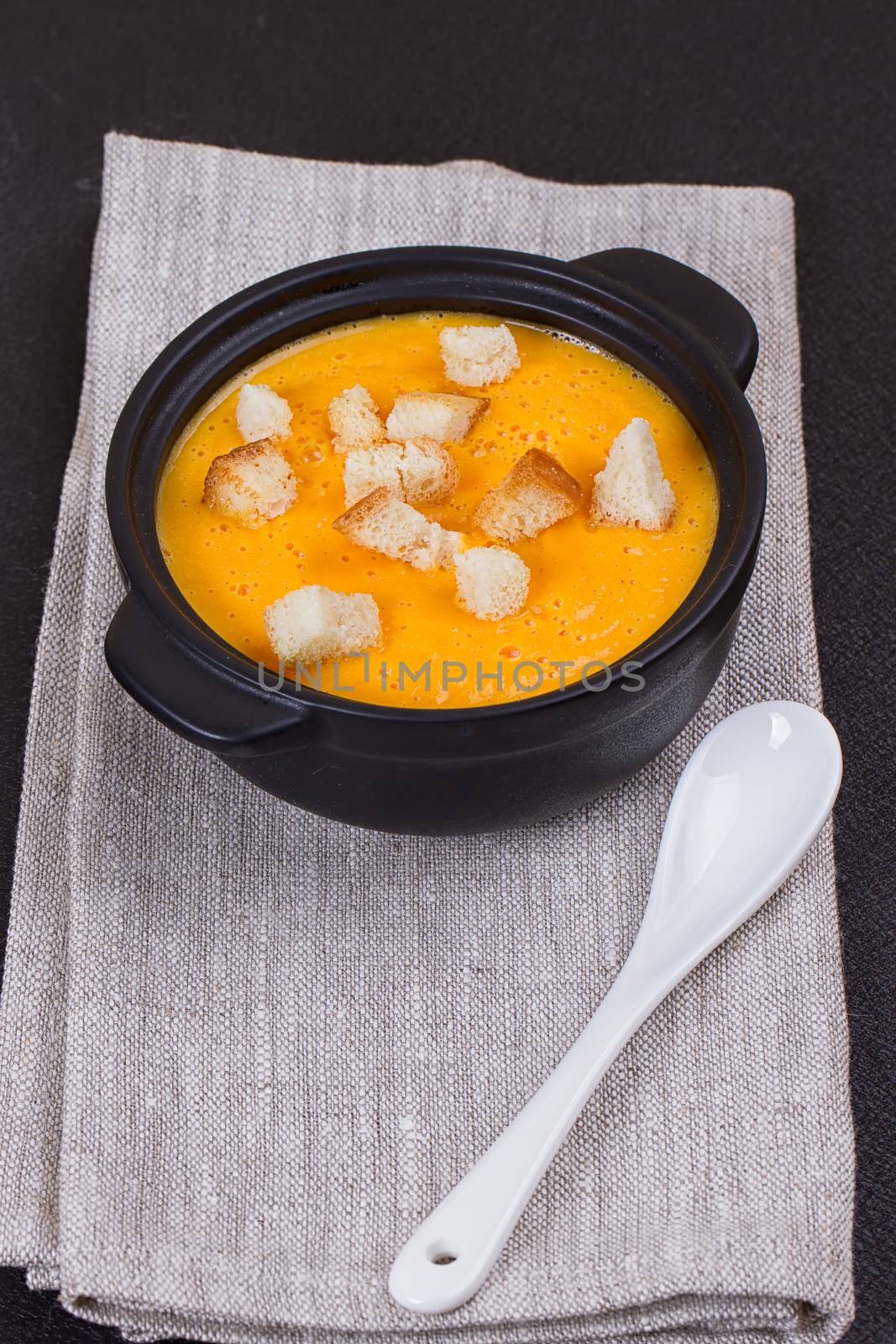 Pumpkin and carrot soup with cream and parsley on dark background Copy space