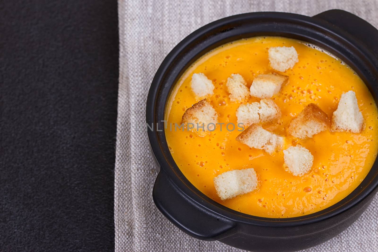 Pumpkin and carrot soup with cream and parsley on dark background Copy space