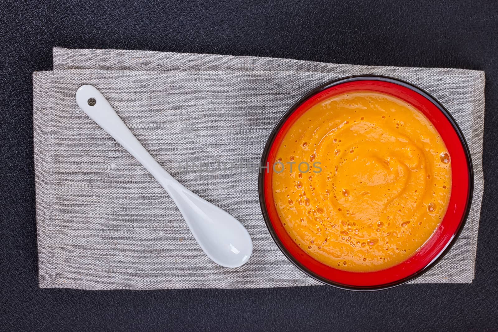 Pumpkin and carrot soup with cream and parsley on dark wooden background