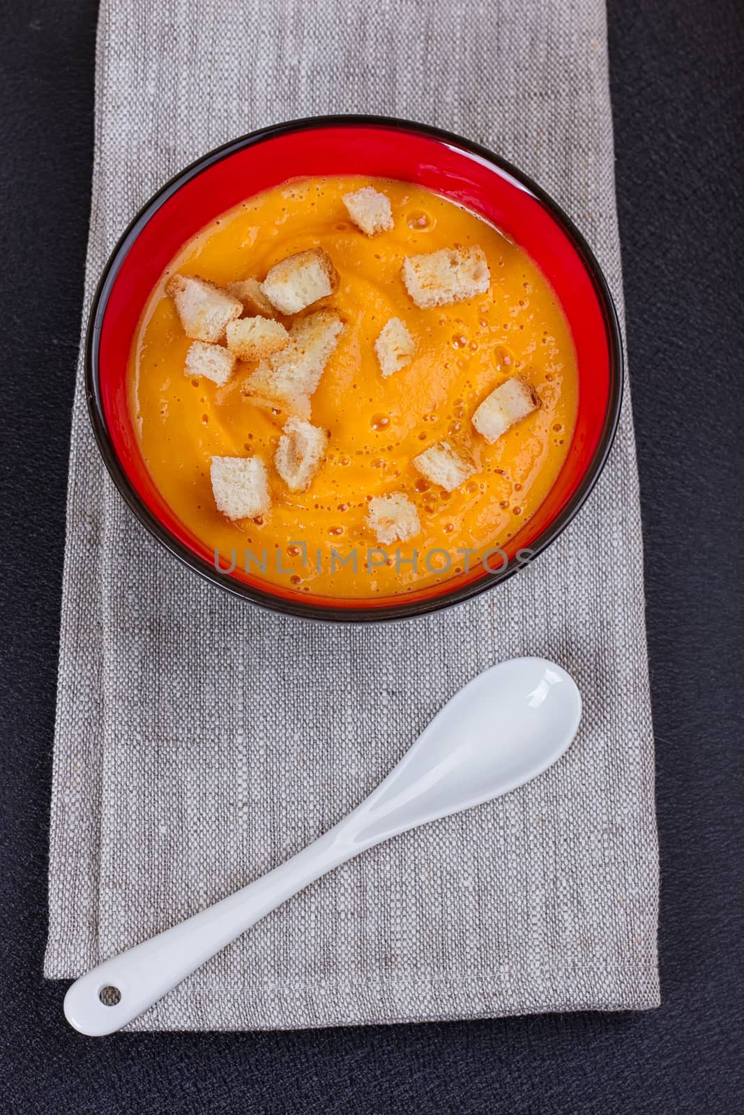 Pumpkin and carrot soup with cream and parsley on dark background