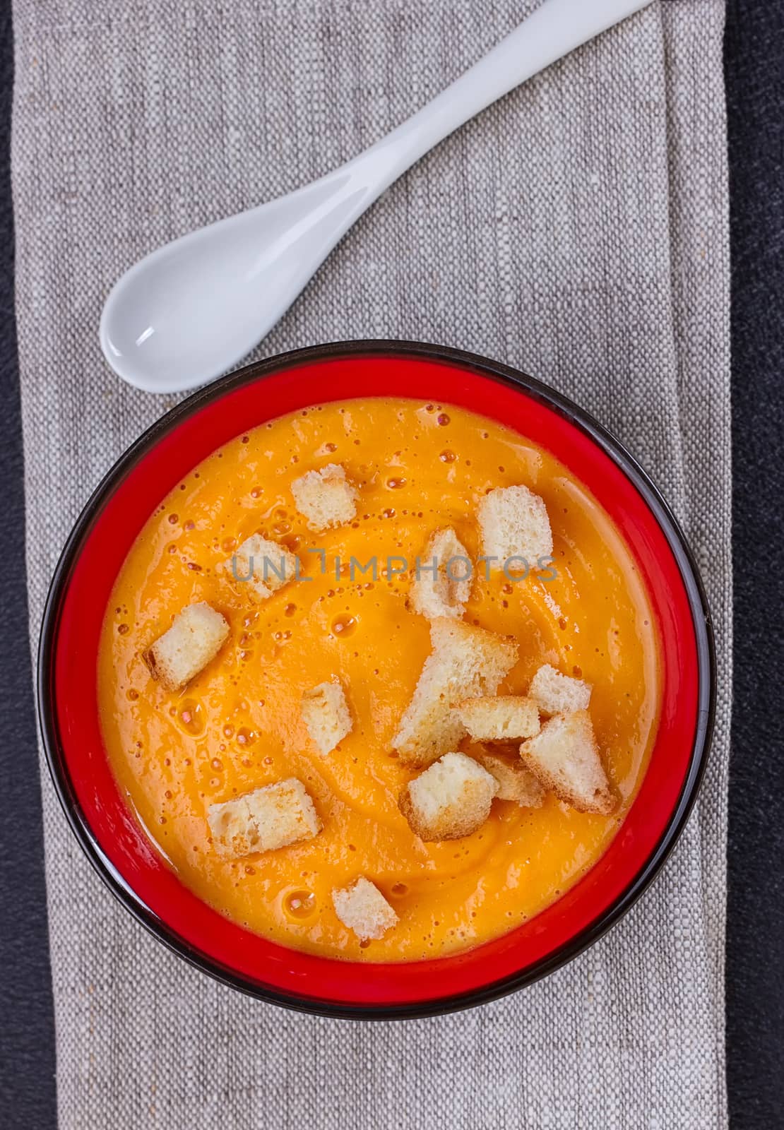 Pumpkin and carrot soup with cream and parsley on dark background