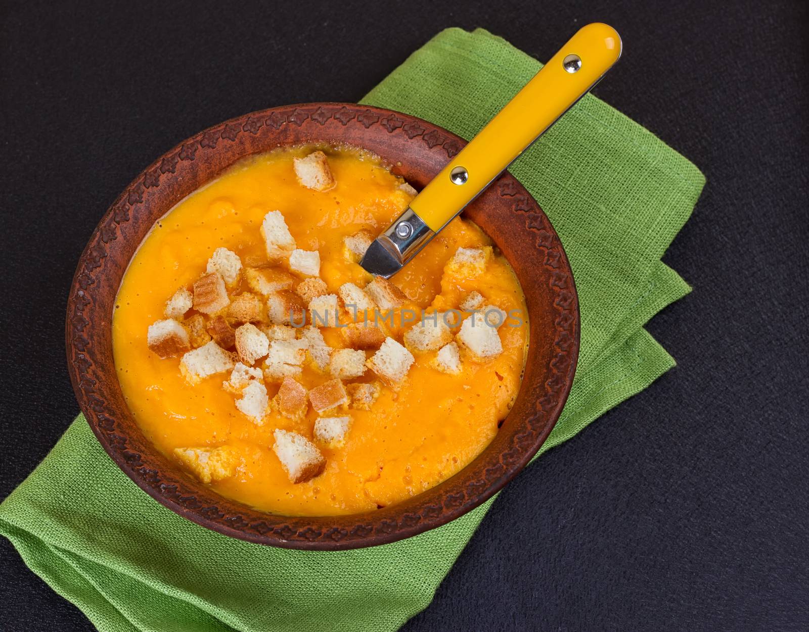 Pumpkin and carrot soup with cream and parsley on dark background