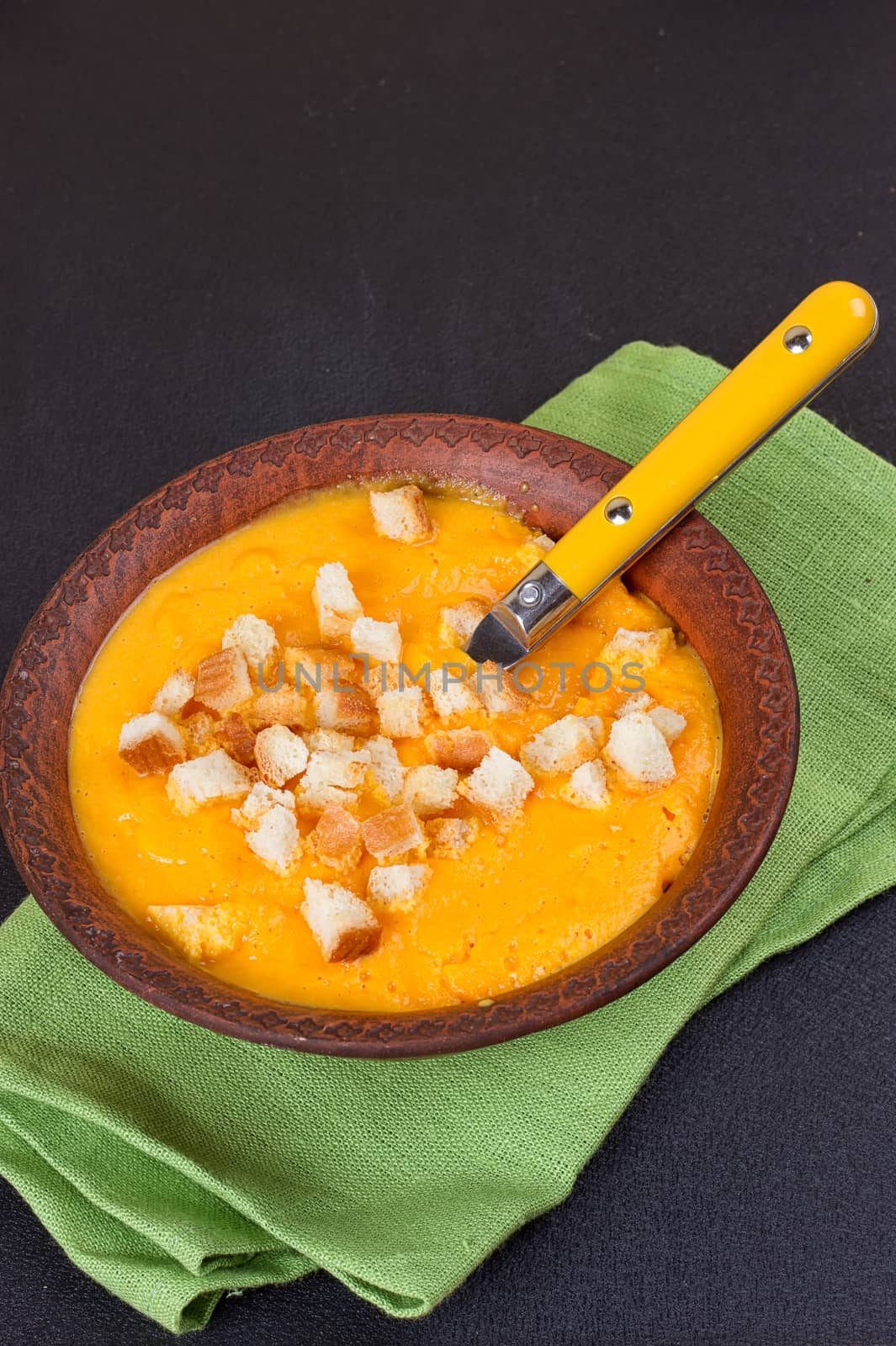 Pumpkin and carrot soup with cream and parsley on dark background