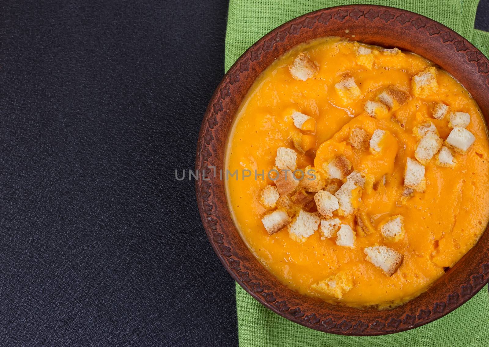 Pumpkin and carrot soup with cream and parsley on dark background Copy space